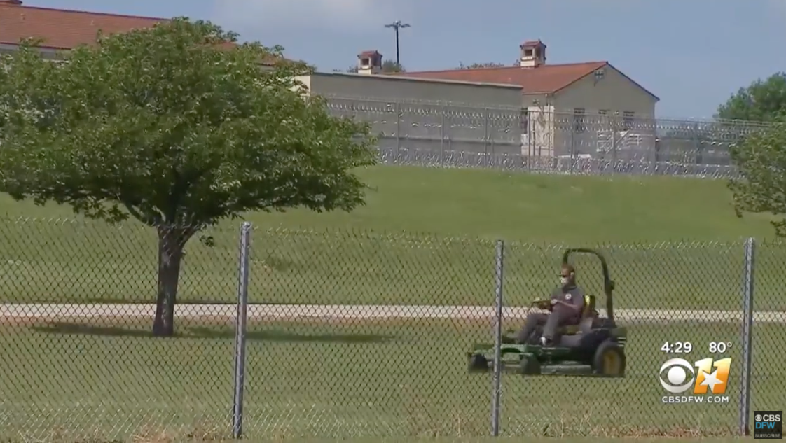a person mowing the lawn outside the prison behind a wired fence