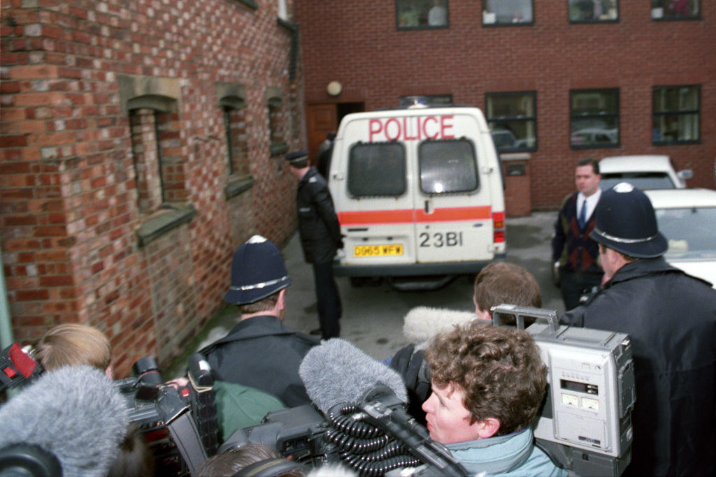 Beverley is taken away by police as a crowd of reporters gathers