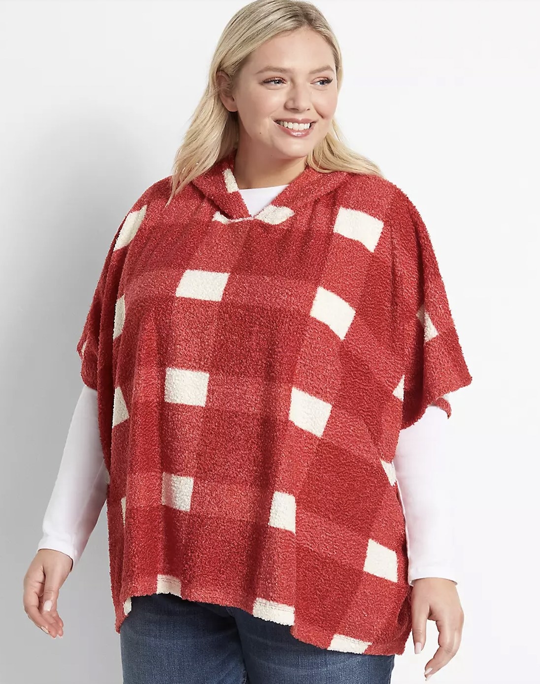 A person wearing a red and white plaid poncho, a white long sleeve shirt, and jeans