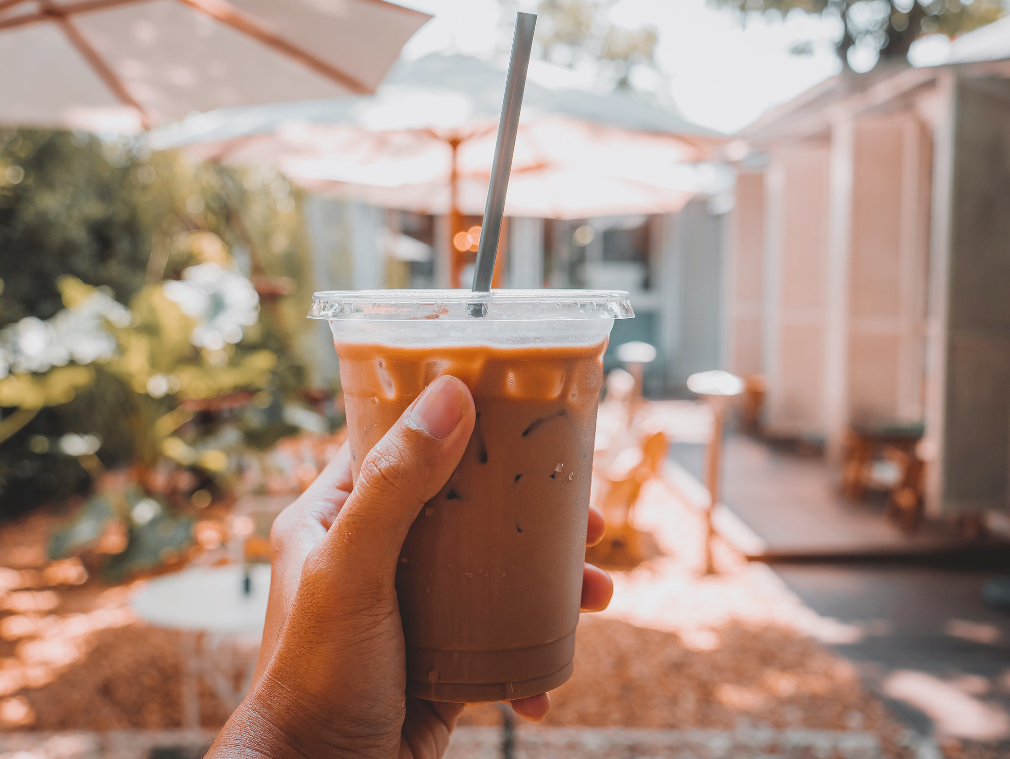 A hand holds a small plastic cup of iced coffee