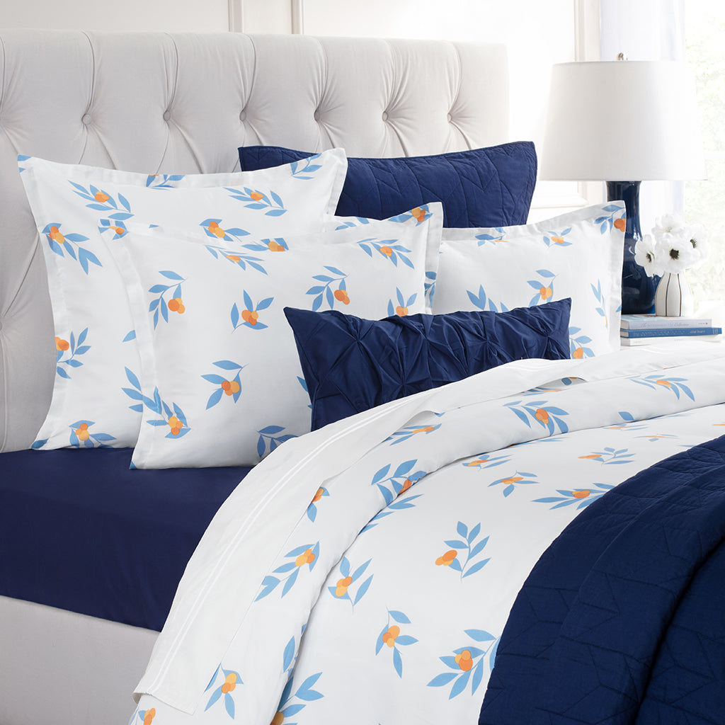 a bed with dark blue bedding and white sheets with light blue leaves on it