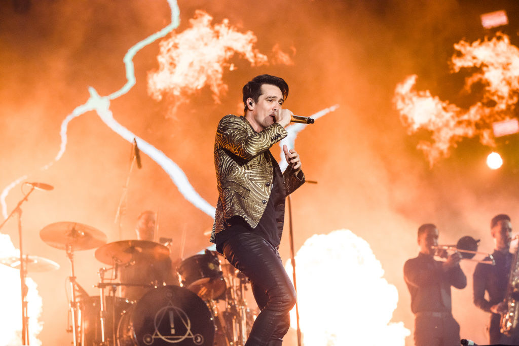 Panic! At The Disco member Brendon Urie sings into a microphone in front of his band during a concert