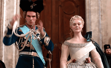 Peter wears a royal overcoat with medals on it and Catherine wears an off the shoulder lightly colored gown