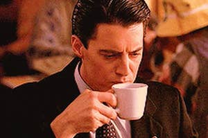A close up of David Lynch as he drinks a cup of coffee