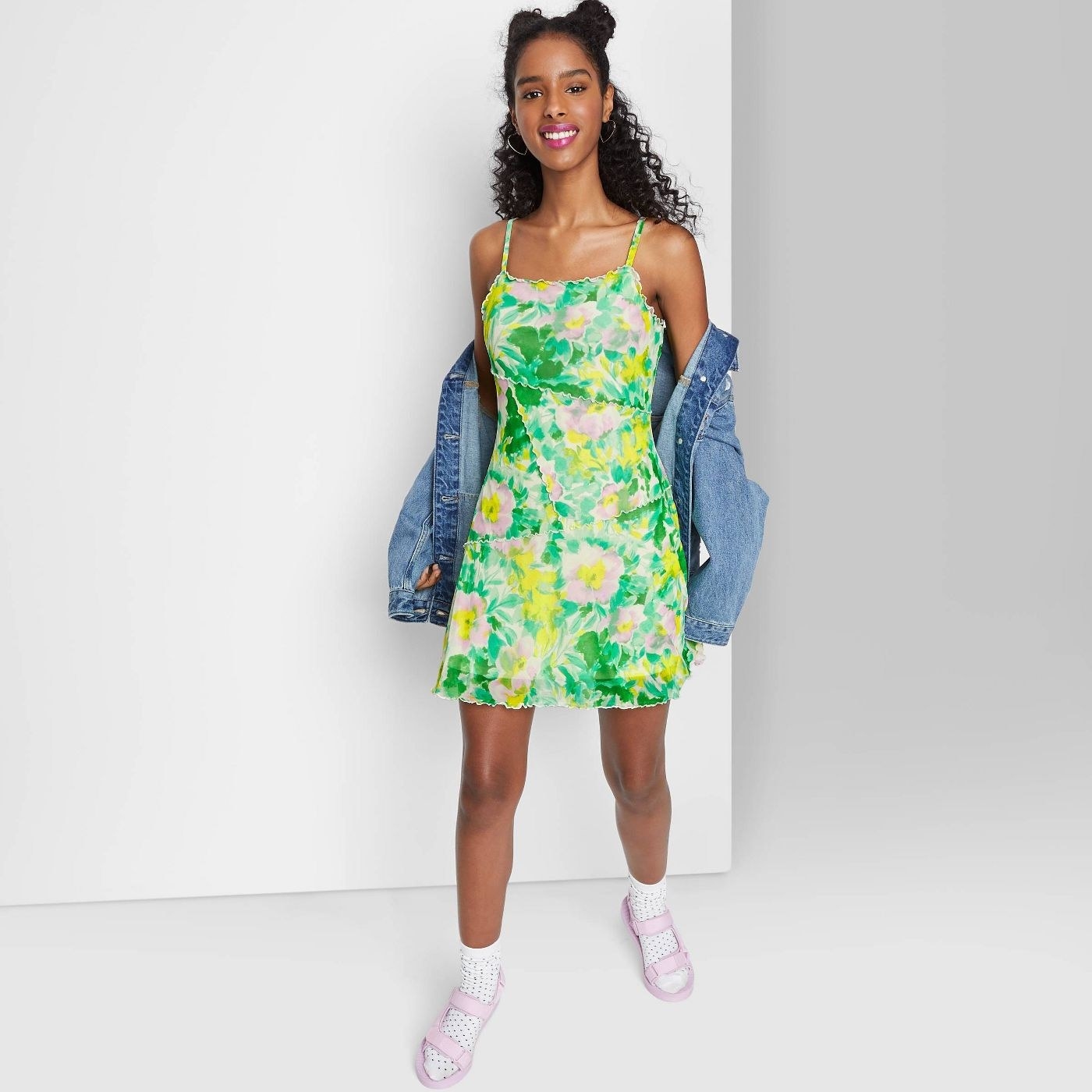 Model wearing green, yellow and pink dress with denim jacket and purple shoes and white socks