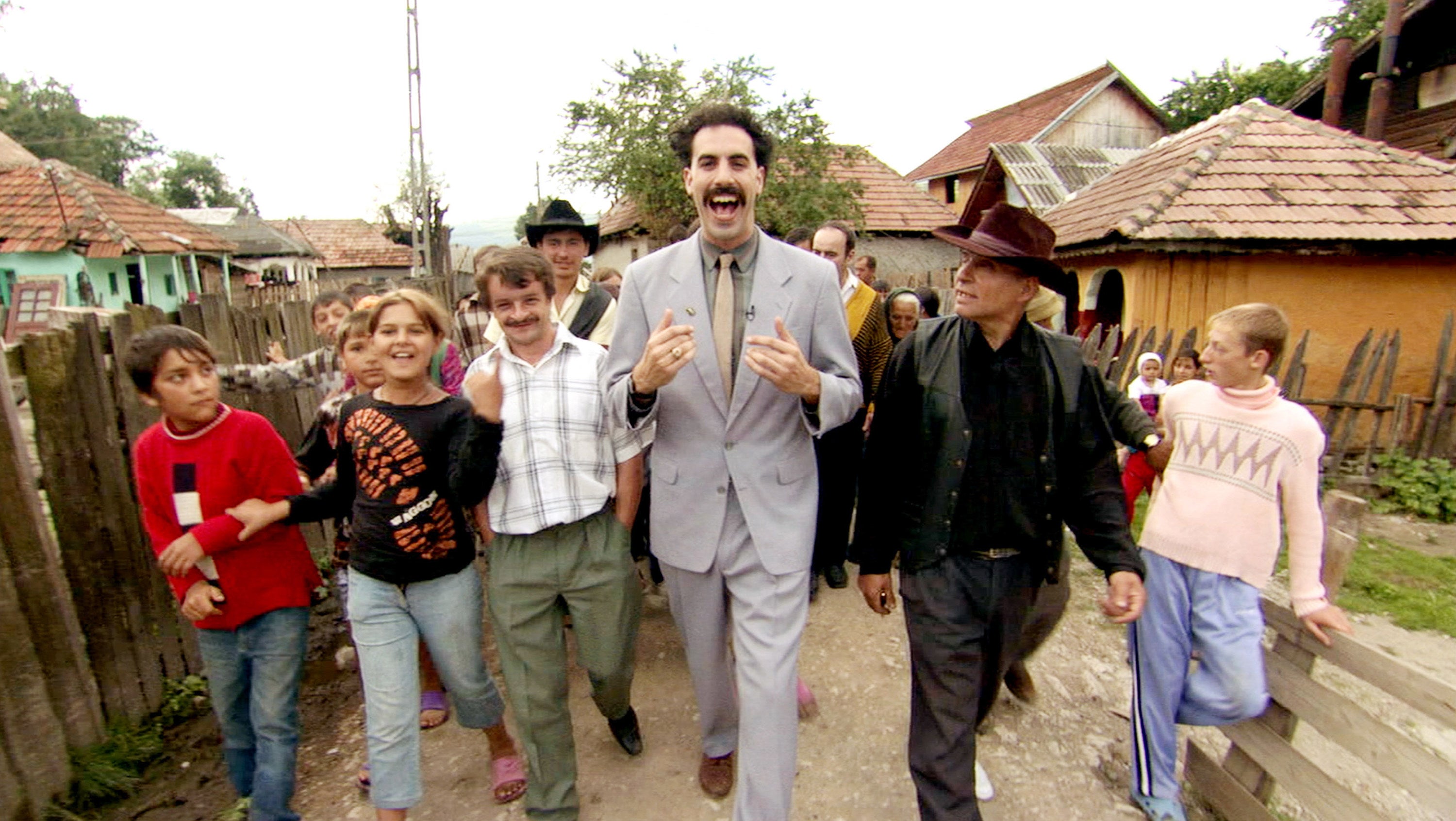 Sacha baron Cohen walks with a bunch of villagers