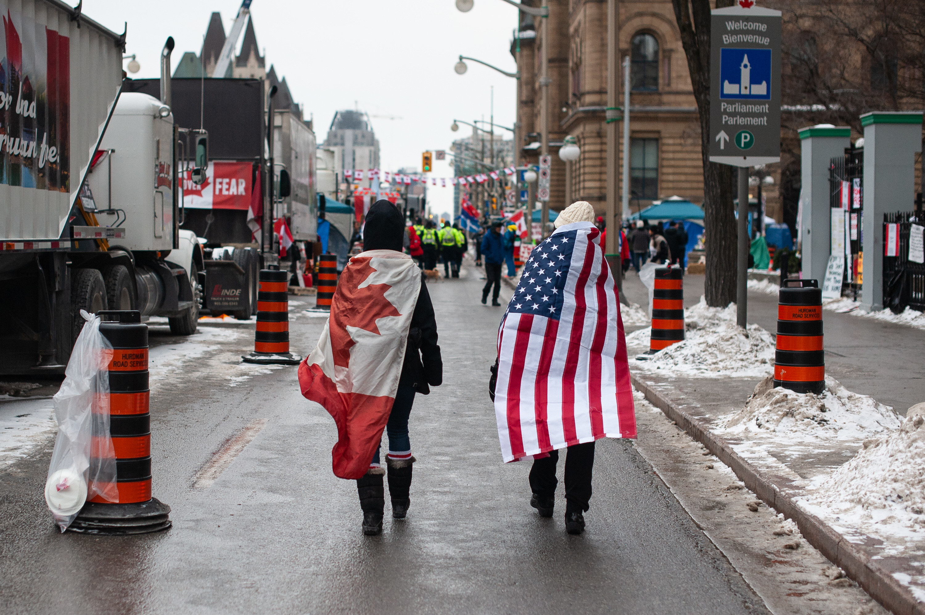 Two people walk with the Canadian and American flags draped across their backs