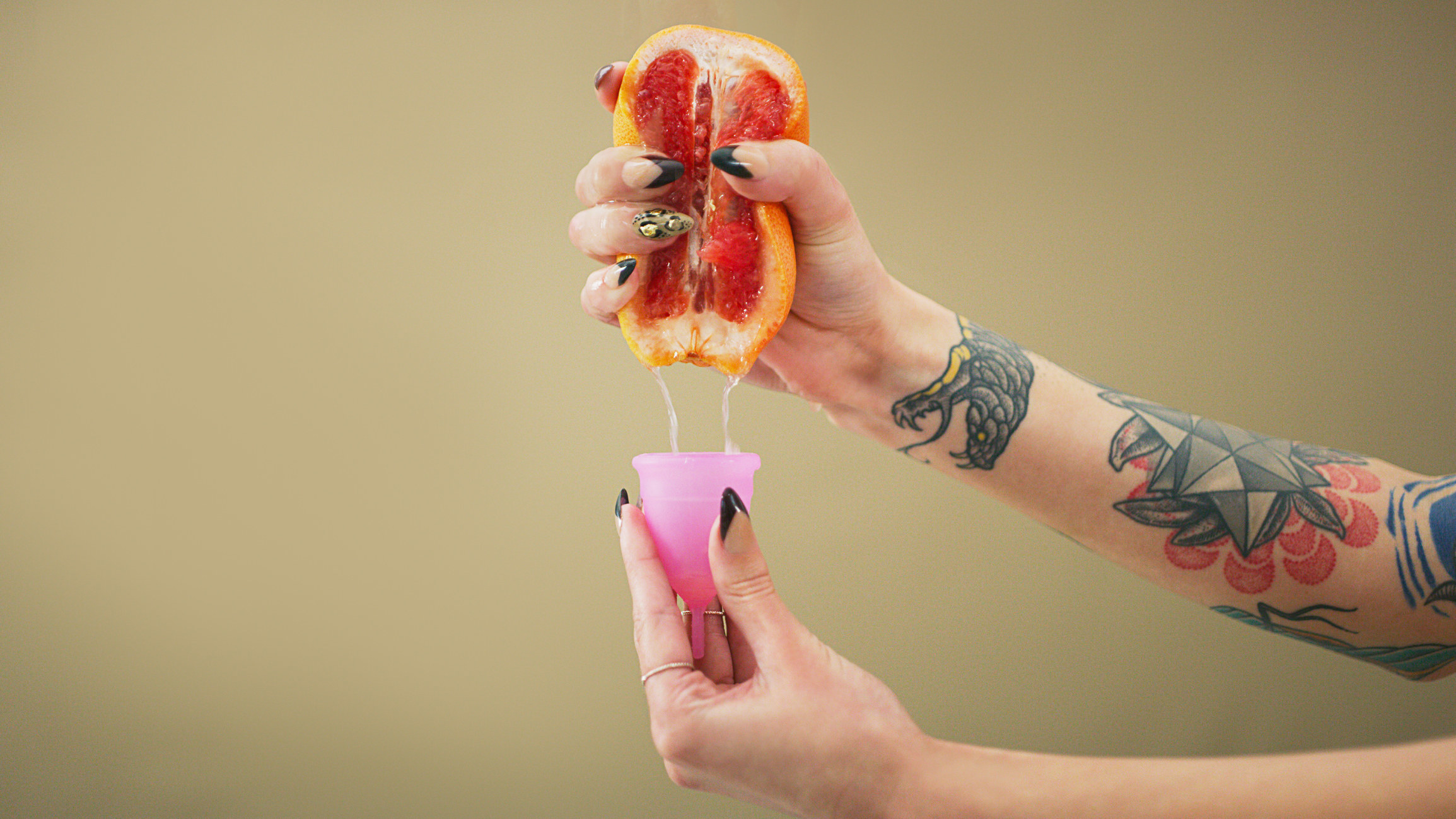 Stock image of a woman holding a menstrual cup in her hand and squeezing the fruit of a grapefruit into said cup
