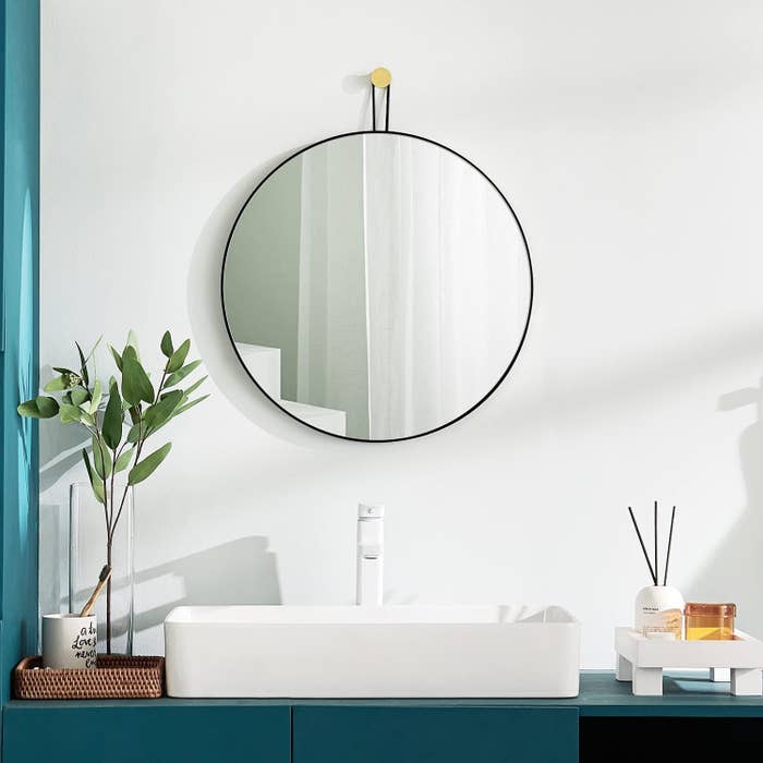 the large circle mirror hanging in a bathroom above a sink