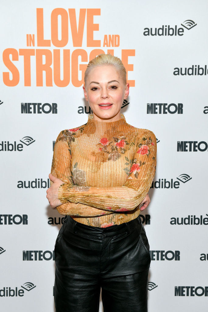 dressed in a sheer floral sweater and leather pants, Rose poses with her arms folded on the red carpet.