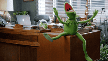 Kermit the frog sitting on a desk cheering