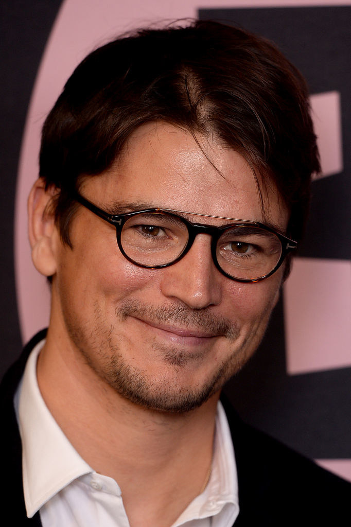 wearing big glasses and a classic suit, the actor smiles at the camera