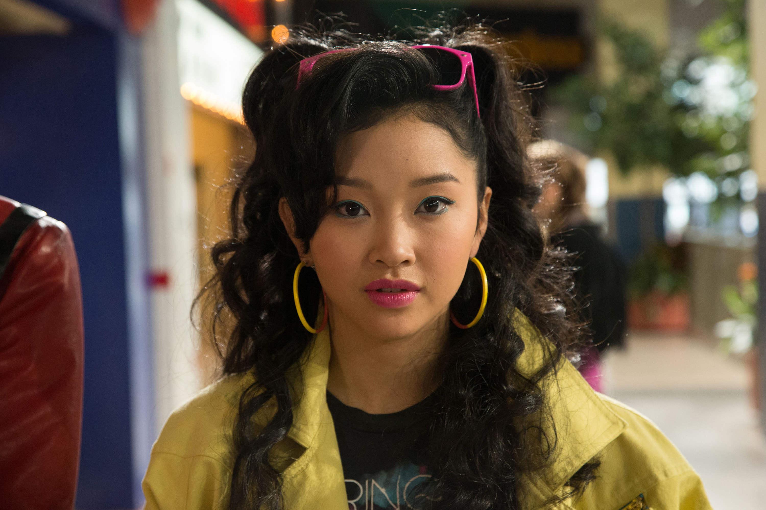 with her curly  hair in pigtails dressed in a bright jacket, sunglasses, and hoop earrings, Jubilee stares into the camera