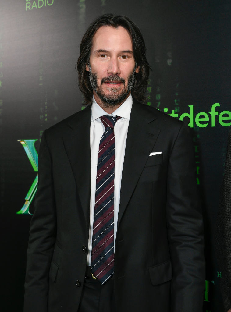 wearing a classic suit and striped tie, Keanu poses on th ered carpet