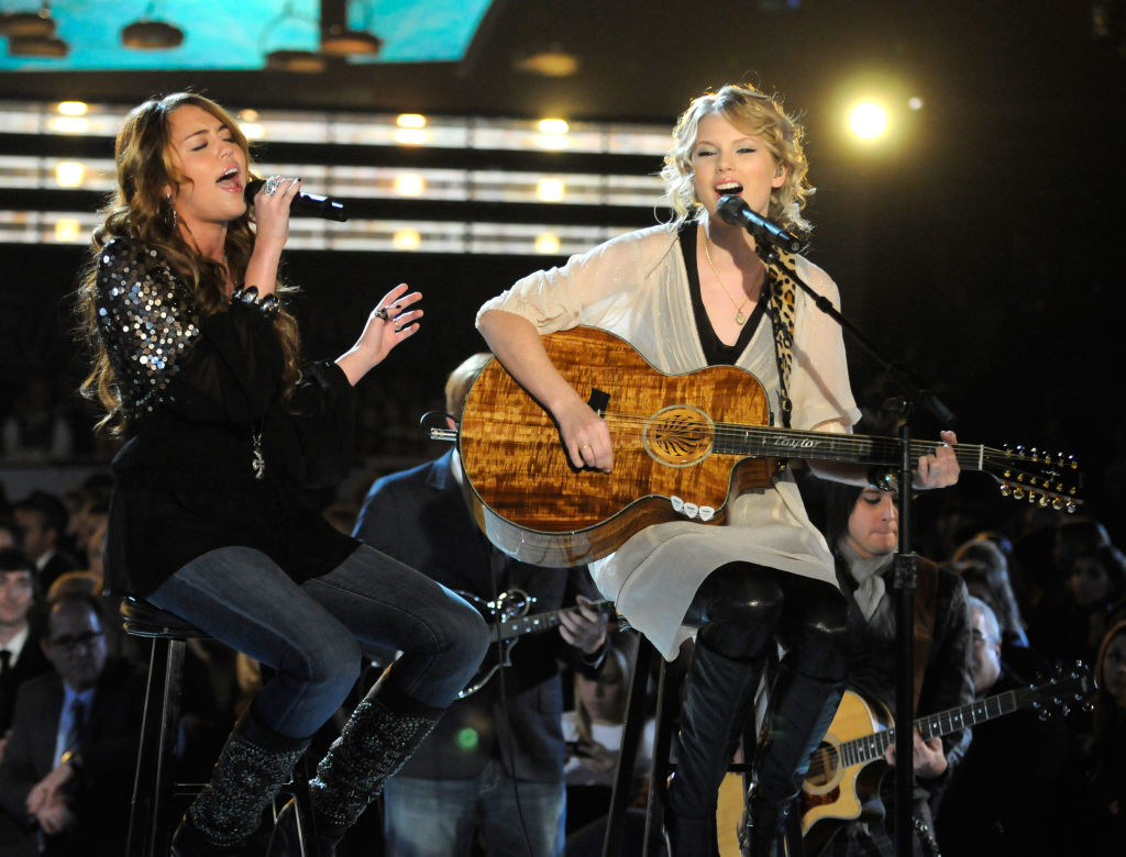 Cyrus and Swift singing while Swift plays an acoustic guitar