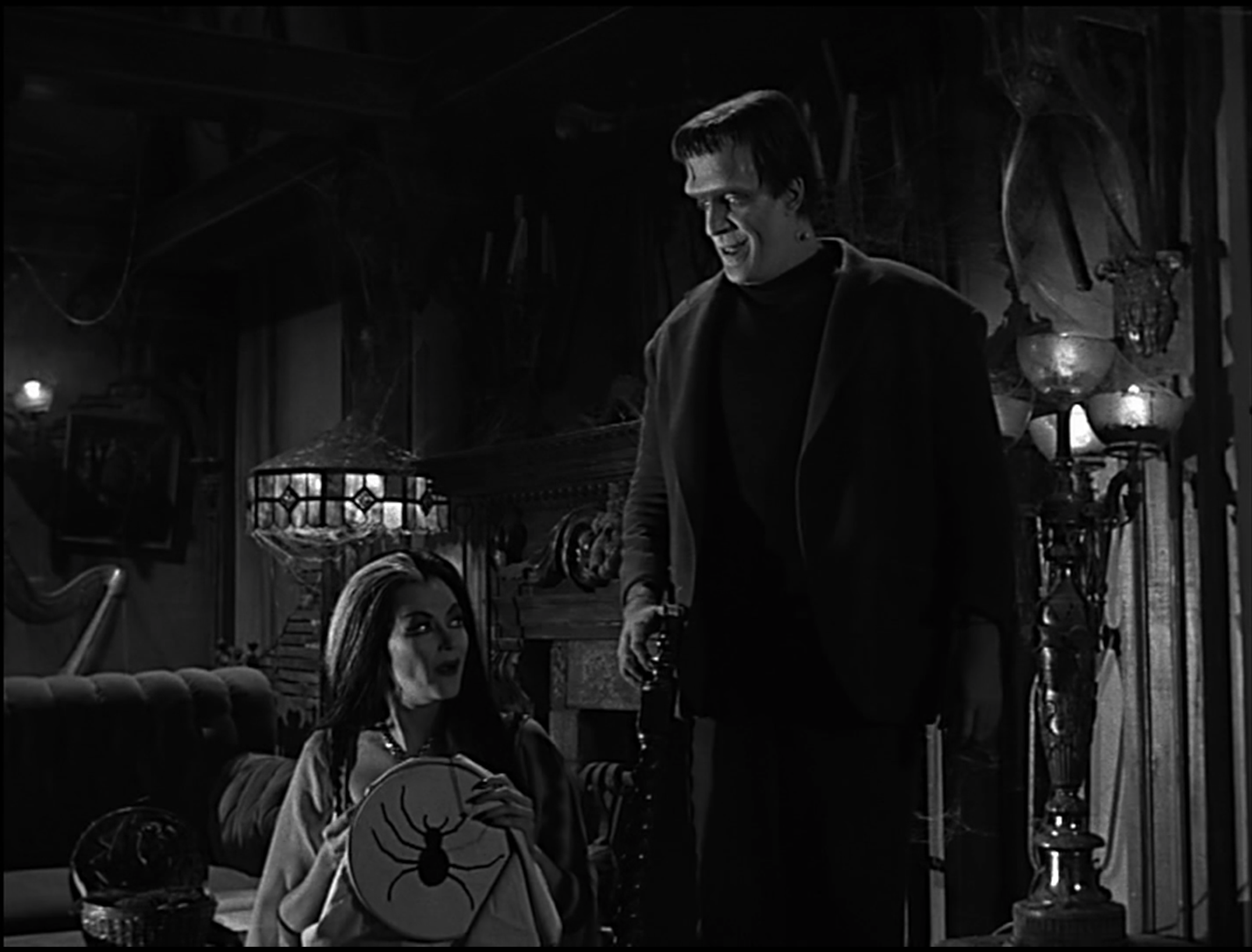 Lily and Herman Munster chat in their living room