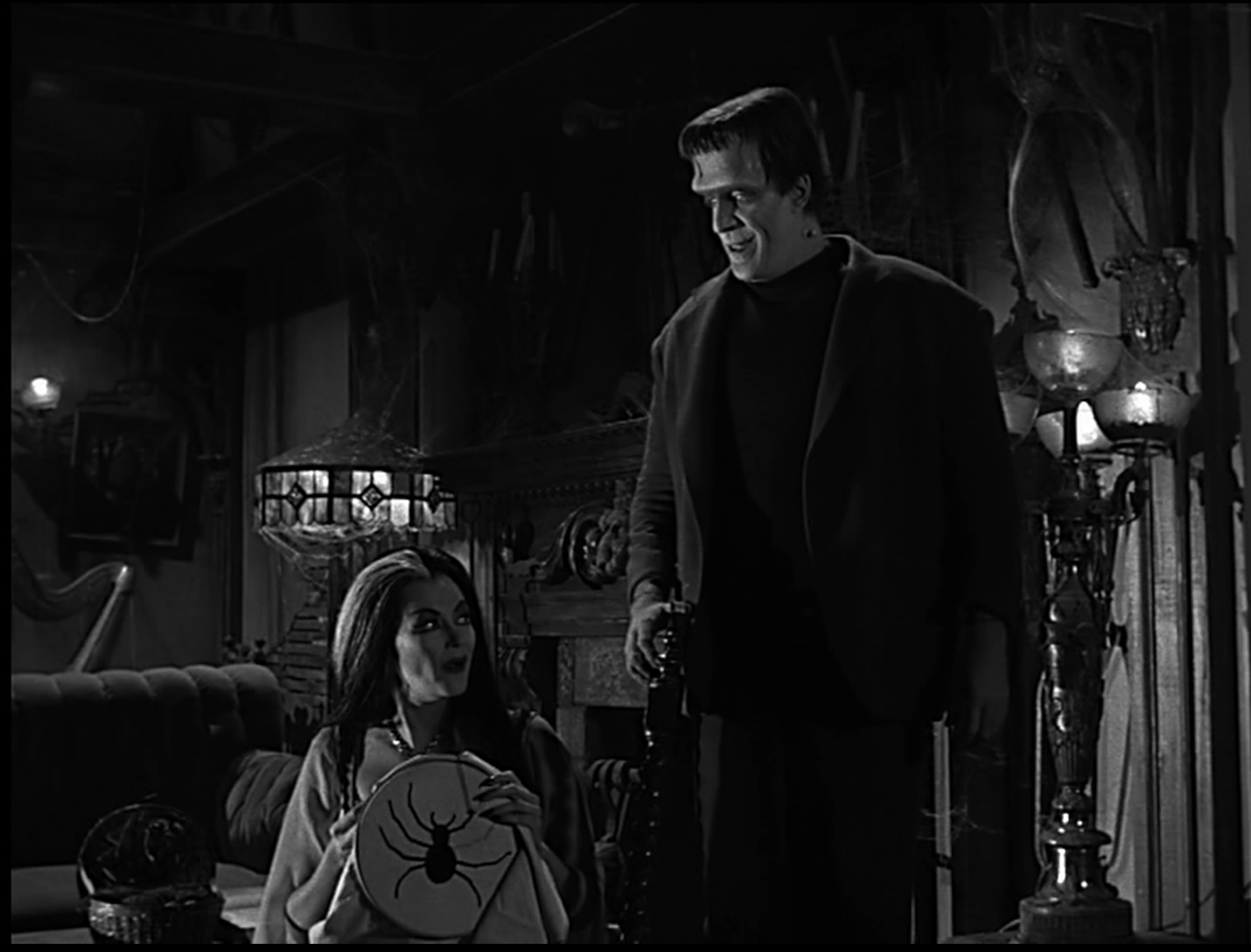 Lily and Herman Munster chat in their living room