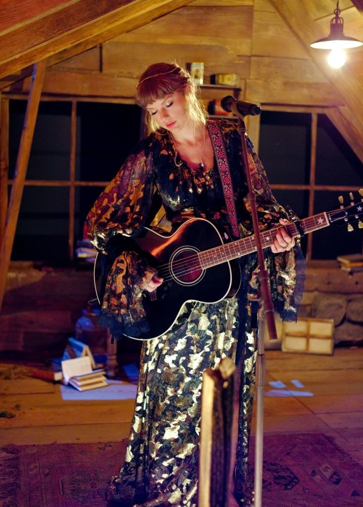 Taylor performing in a cabin with an acoustic guitar