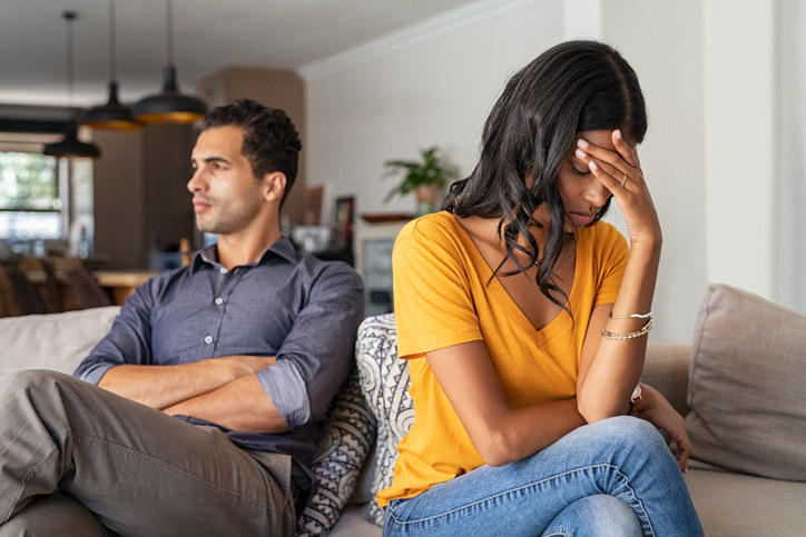 Couple sitting on the couch, facing away from each other in frustration and stress