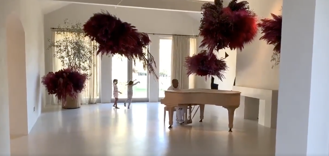 The piano room where Kanye sits at the piano with two children in the back; decorated with red feathers