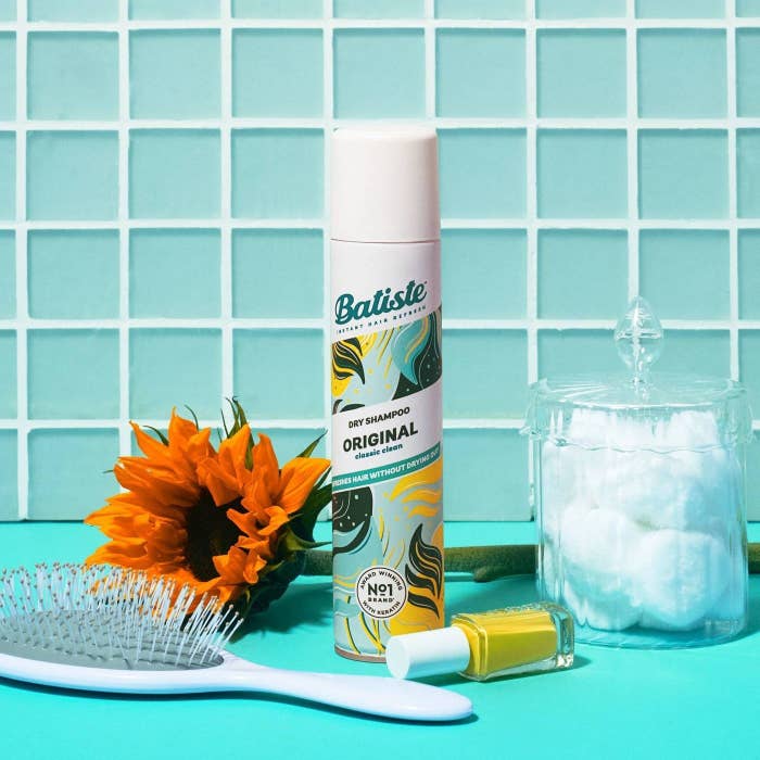 A bottle of blue, green and yellow dry shampoo on blue table with a blue brush, sunflower, yellow nail polish and jar of cotton puffs