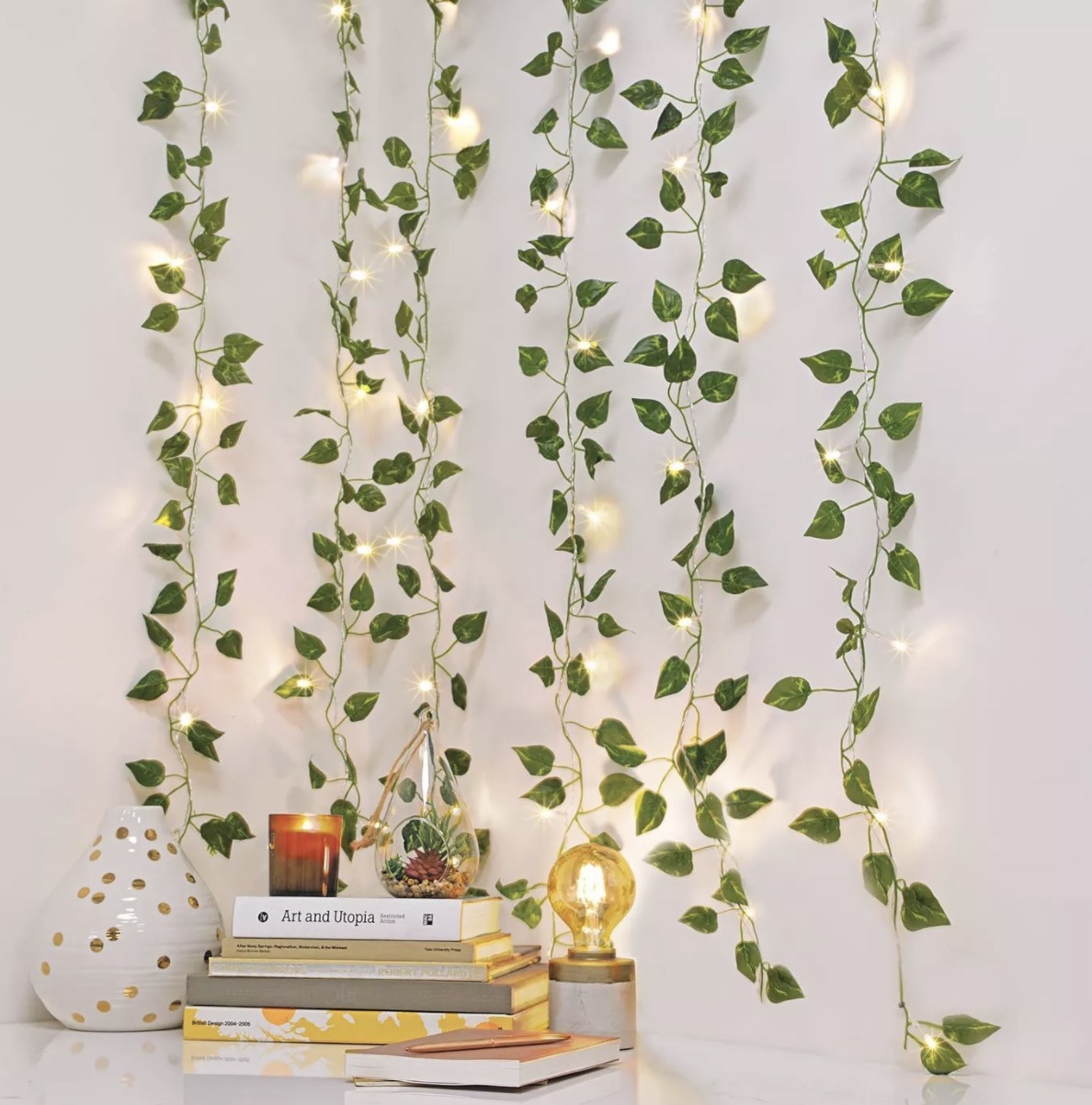 There are six hanging strings of lighted vines in a white room