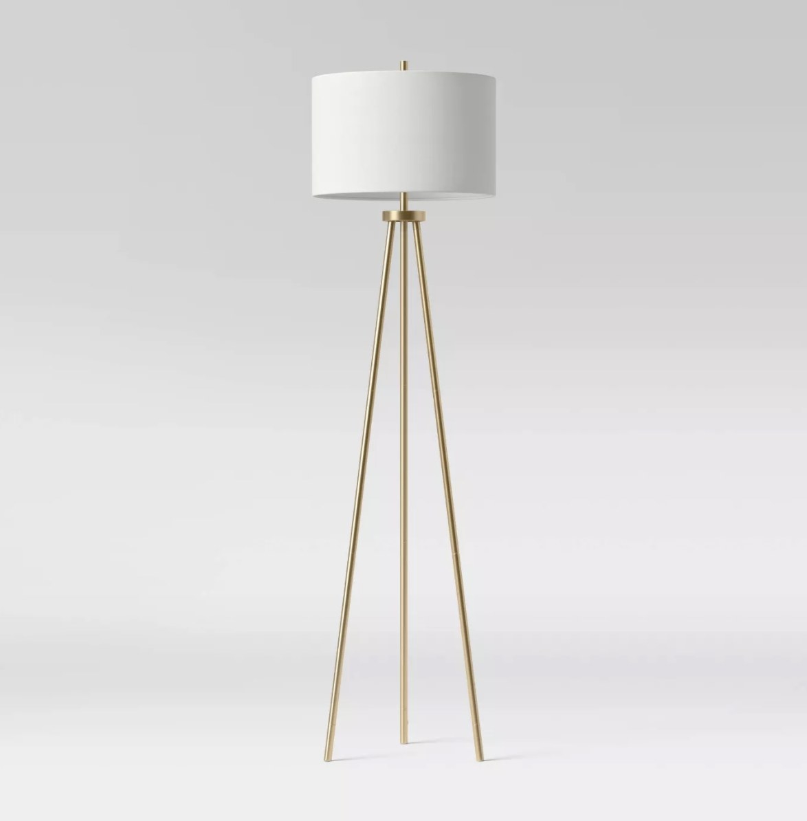The white lamp has a crisp cylindrical shade and three long gold legs