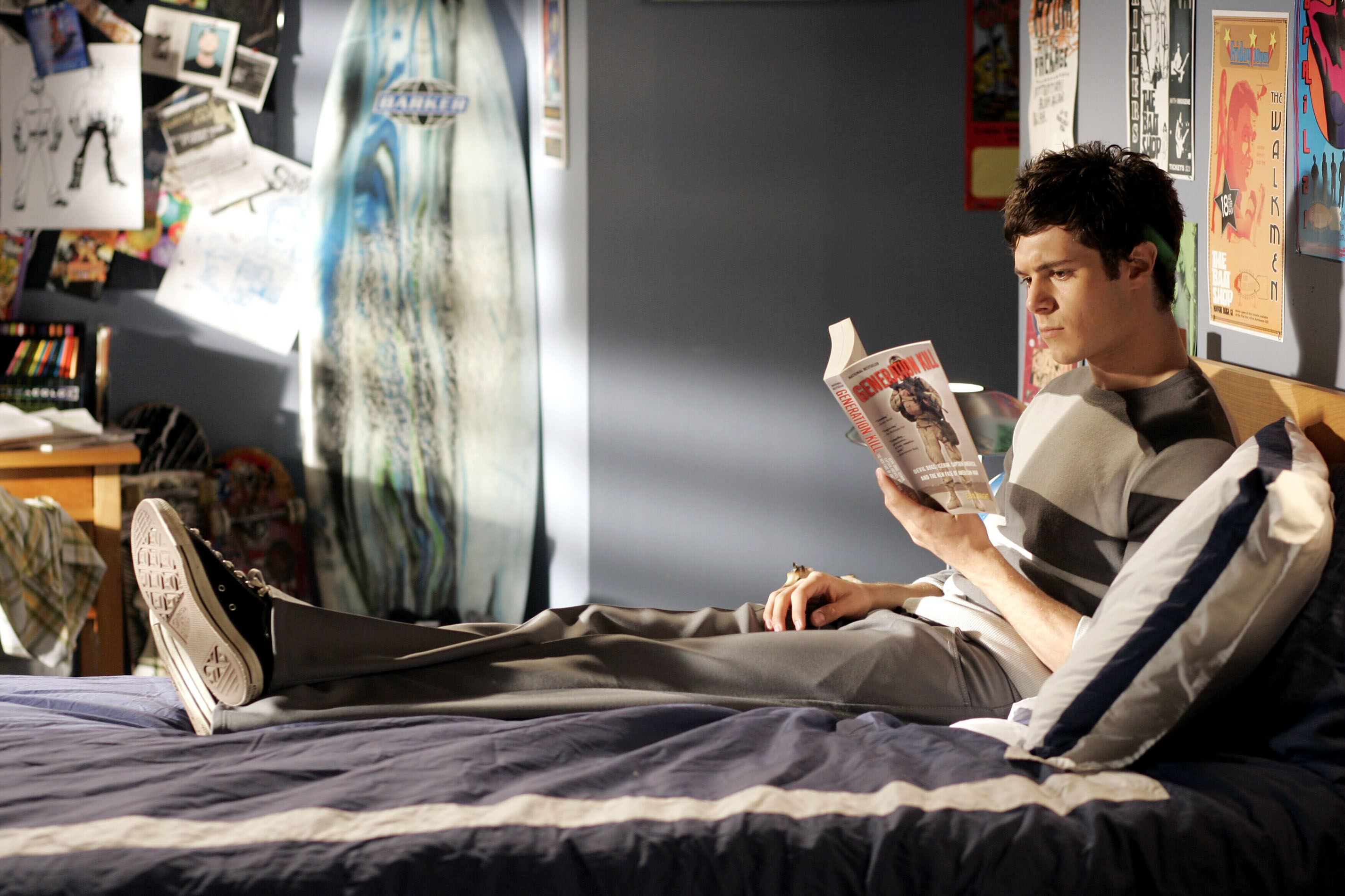 Teen boy reading a book in bed with his shoes on