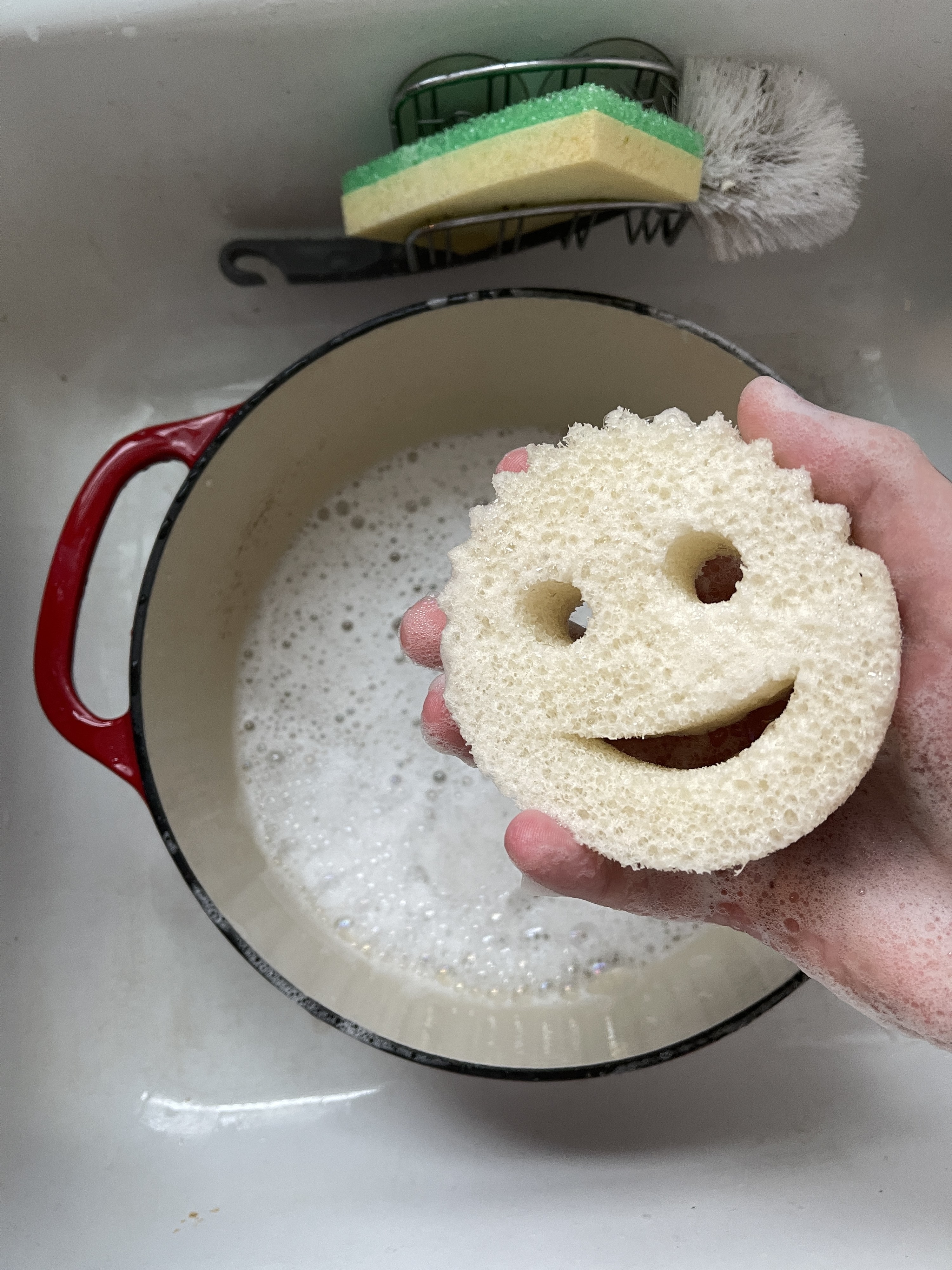 Holding a scrub daddy sponge over a dirty Dutch oven in the sink