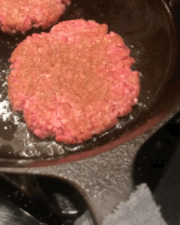 Author cooking smash burgers in a cast iron skillet