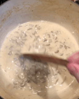 Author stirring creamy mushrooms with a wooden spatula