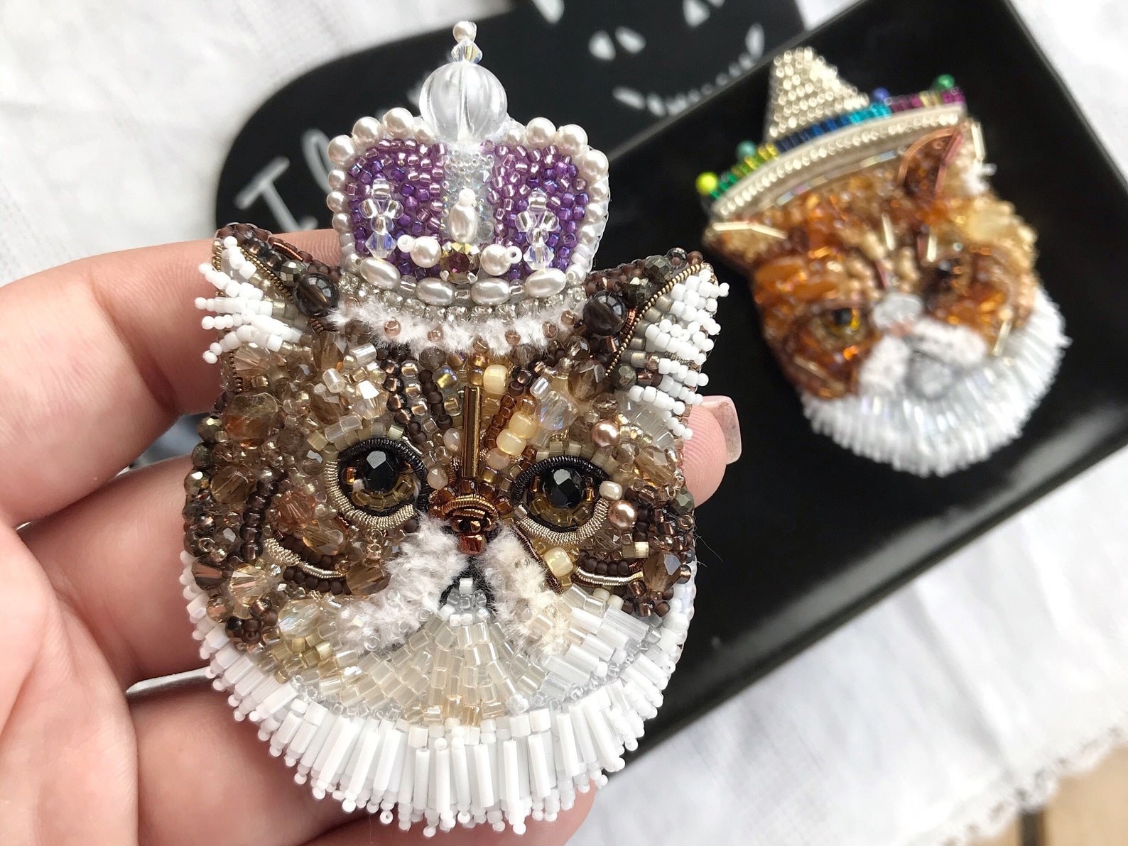 A person holding one of the custom brooches of a cat