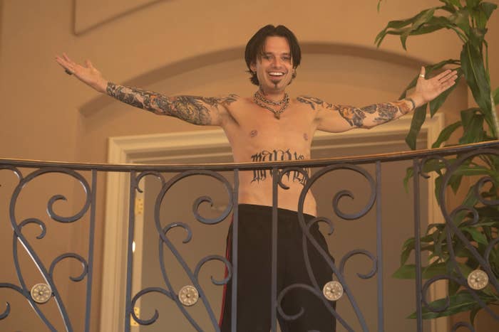 Sebastian as Tommy with his arms outstretched as he smiles while standing on a balcony