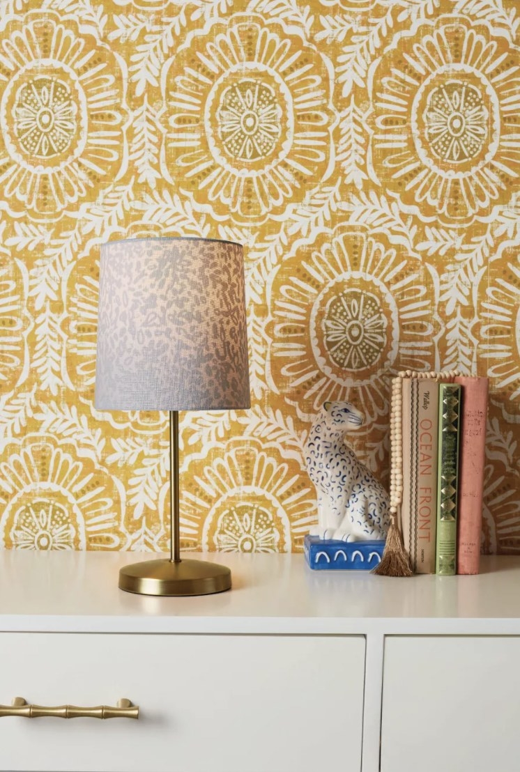 The yellow wallpaper has medallion and floral patterns and is stuck to a wall behind a modern dresser