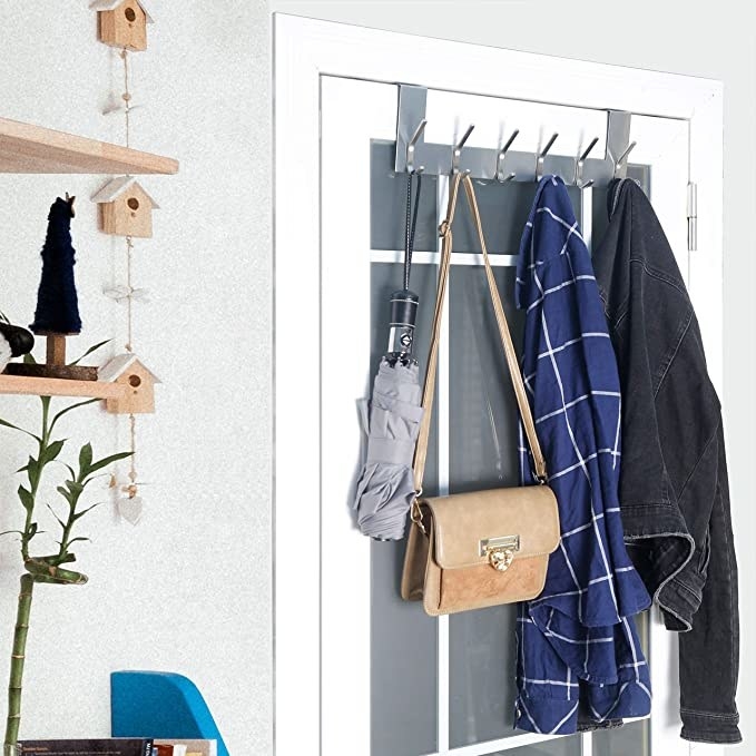 An over-the-door hook holding a denim jacket, plaid shirt, purse, and umbrella in a room