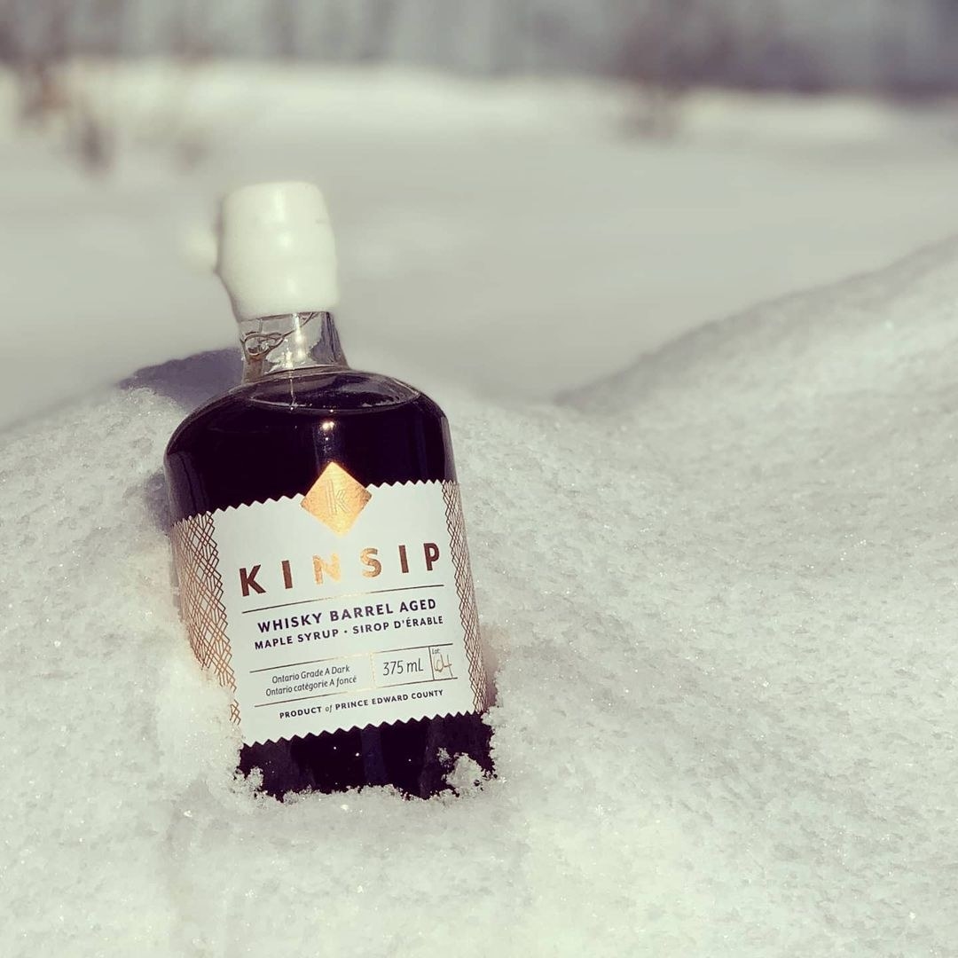 a bottle of whiskey barrel aged maple syrup nestled in a snow bank