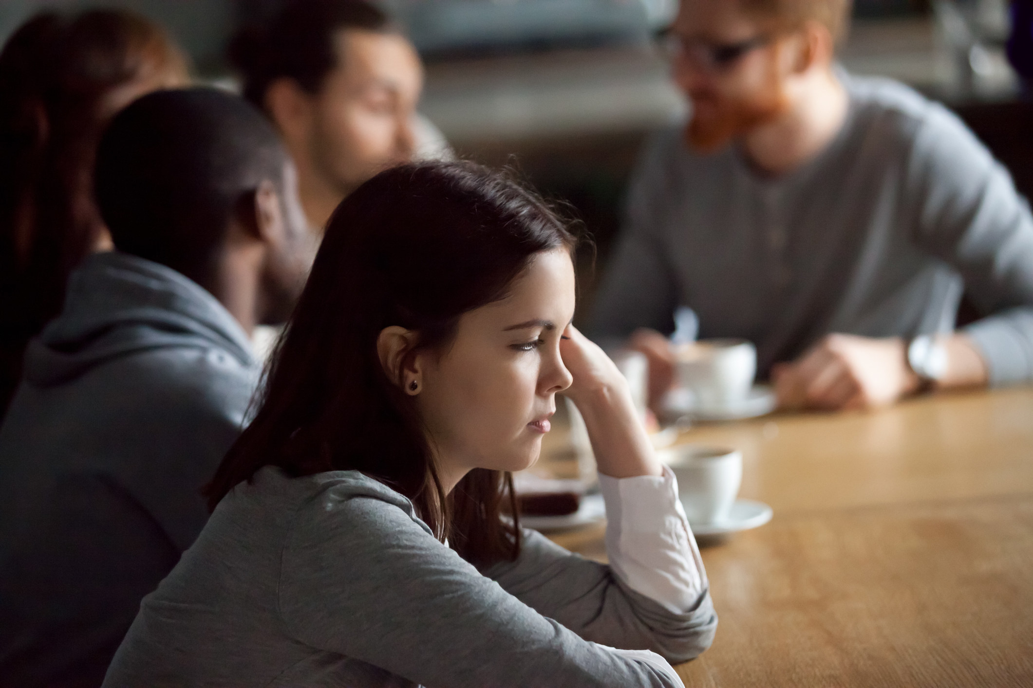 A stock image of a woman sitting alone staring ahead as a group of people talk beside her
