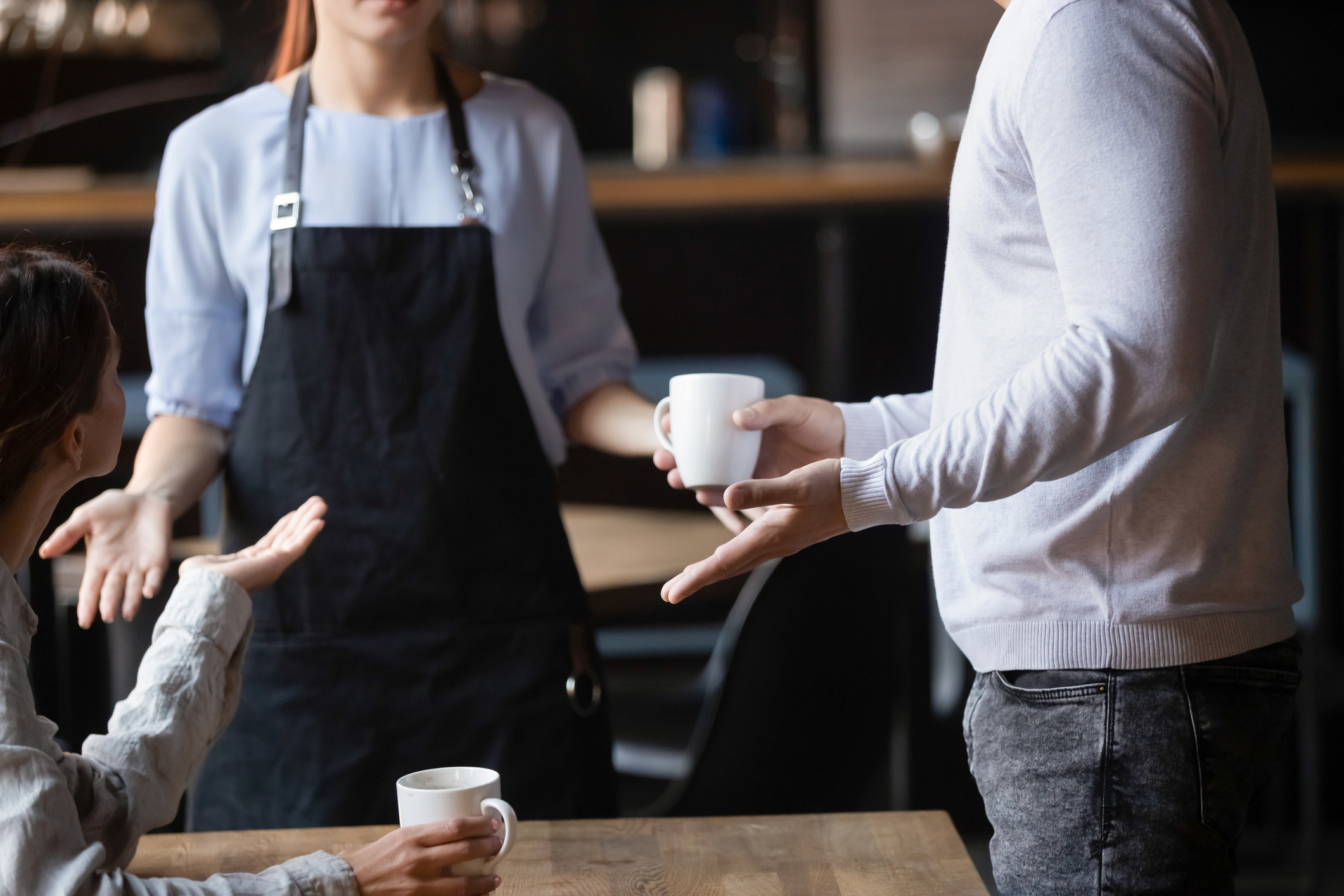 A stock image of two customers at a table holding their hands up as a worker stands in front of them