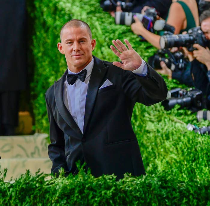 Tatum waves to a crowd while standing behind bushes lining the red carpet of an event