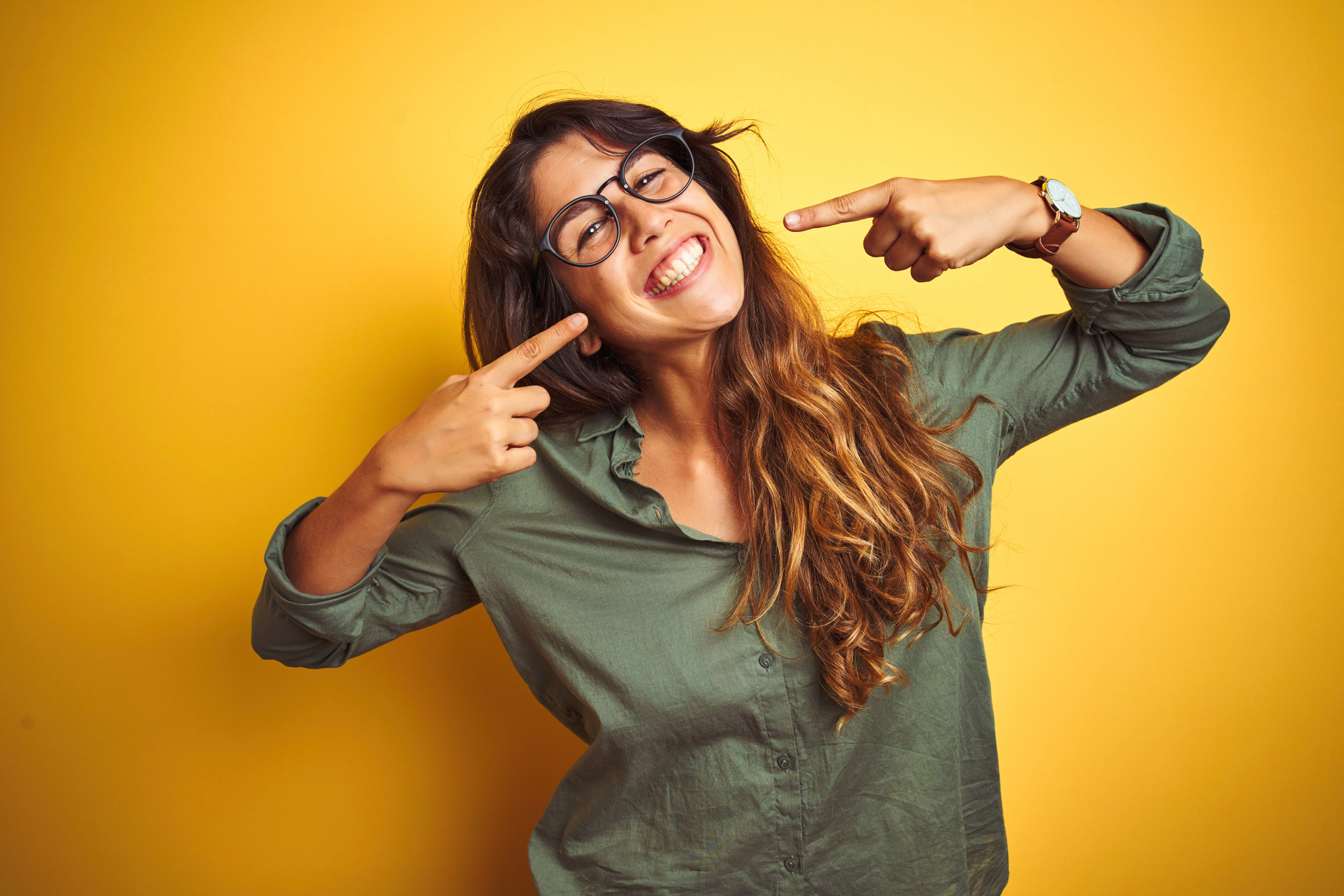 A stock image of a woman smiling while using her hands to point to her smile
