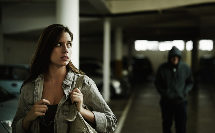 A terrified young woman in an underground parking garage being followed by a sinister man