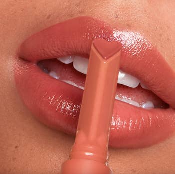 Close-up of lips, showing off juicy, shiny, and peachy pink color and the heart-shaped gloss stick