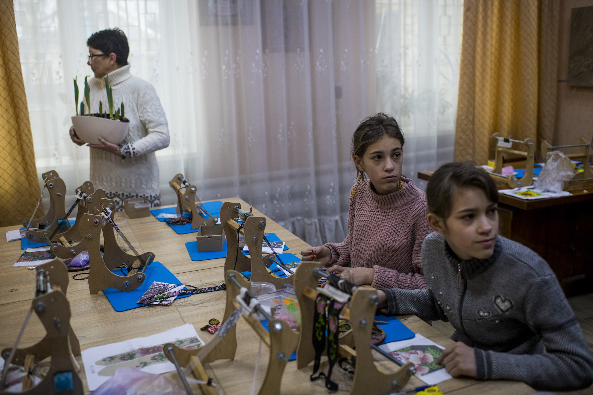 Two children sit at a table as a woman stands nearby