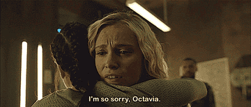 Marie Avgeropoulos as Octavia, and Eliza Taylor as Clarke hugging, and saying &quot;I&#x27;m so sorry, Octavia&quot;