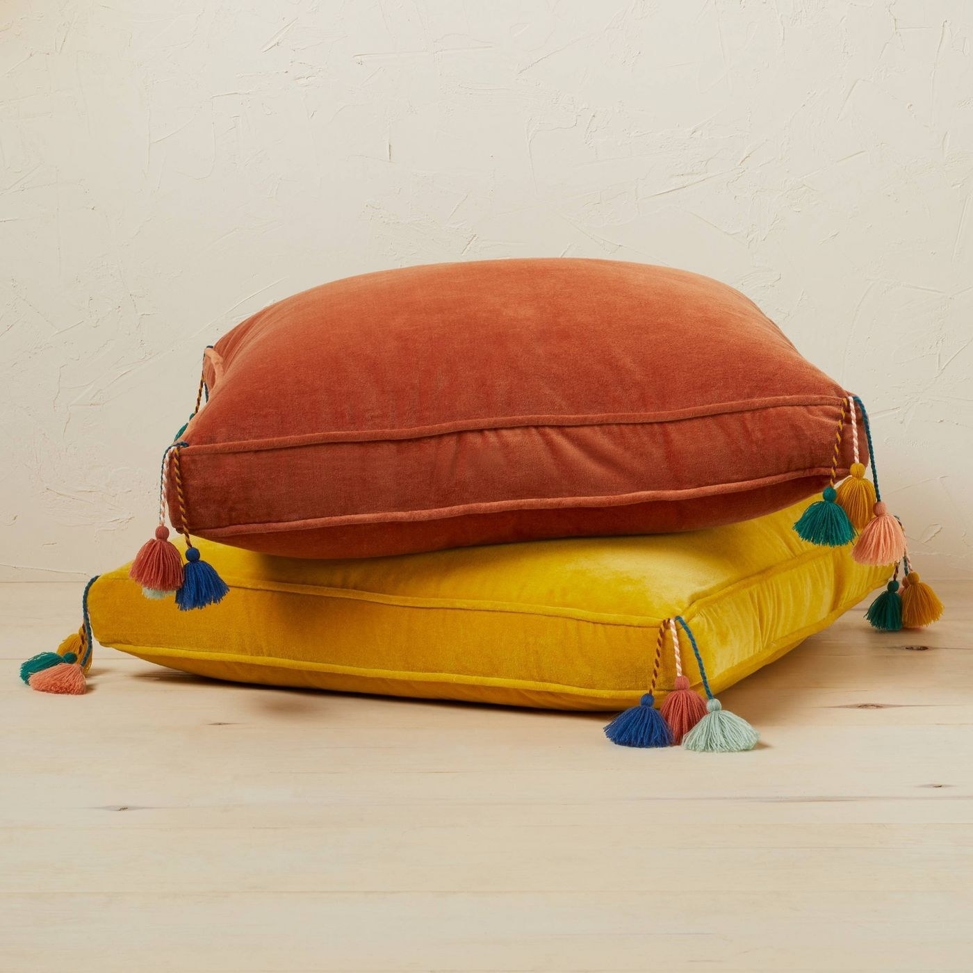 two square floor pillows with corner tassels in yellow and orange