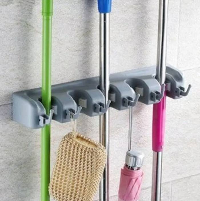 A wall-mounted cleaning supply bracket holding mops, brooms, etc