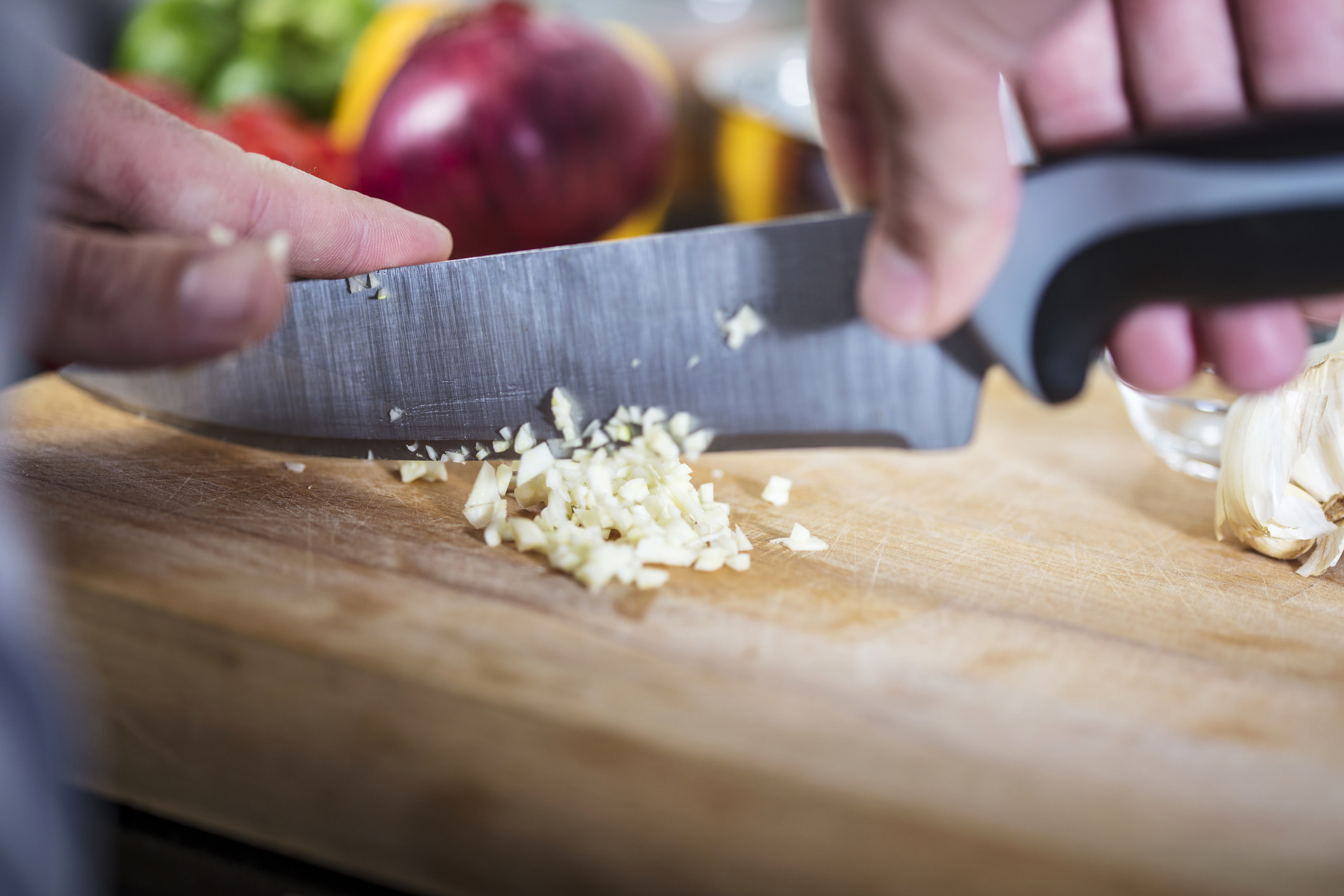 A stock image of hands chopping fresh garlic on a cutting board