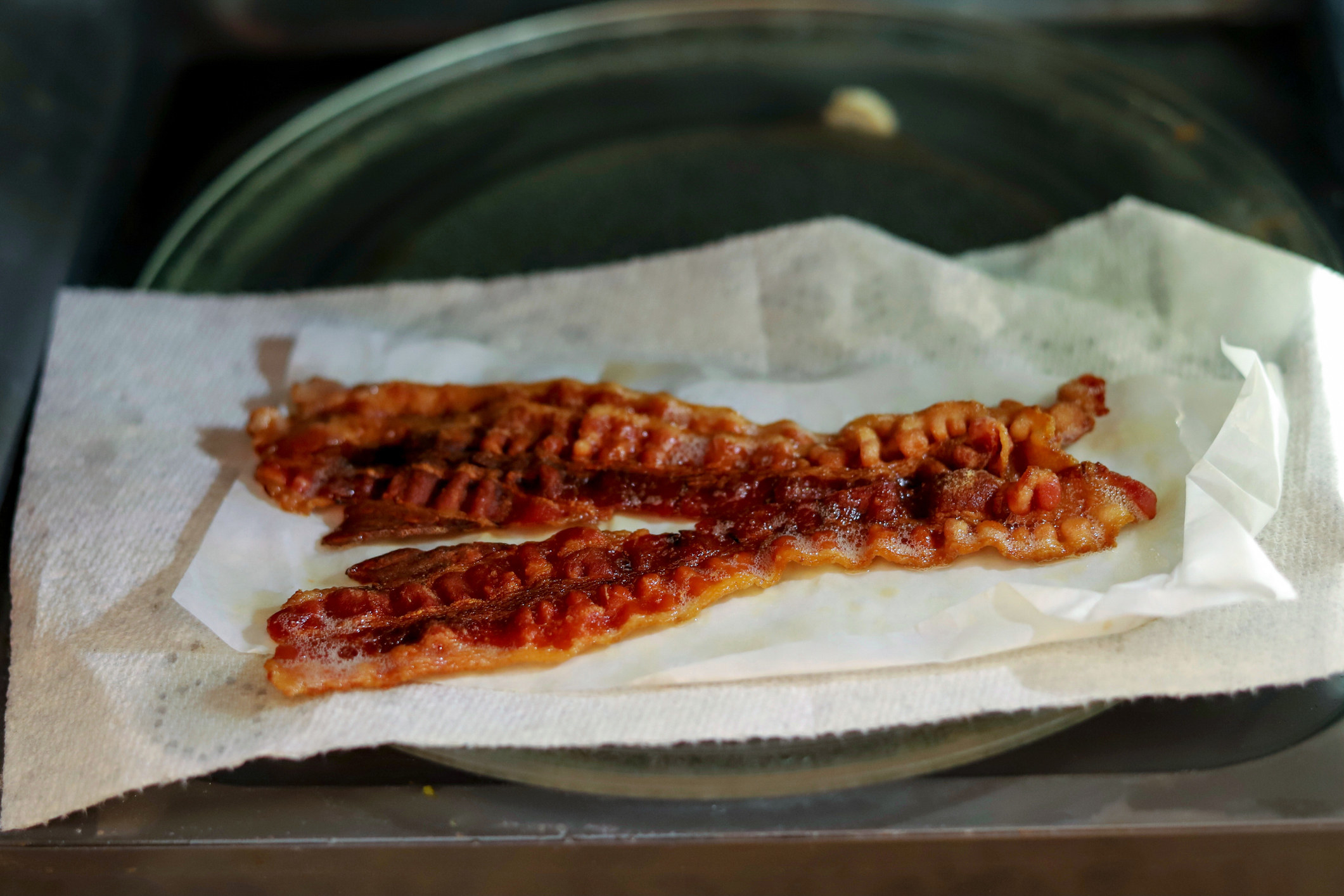 A stock image of cooked bacon inside a a microwave sitting on paper towels