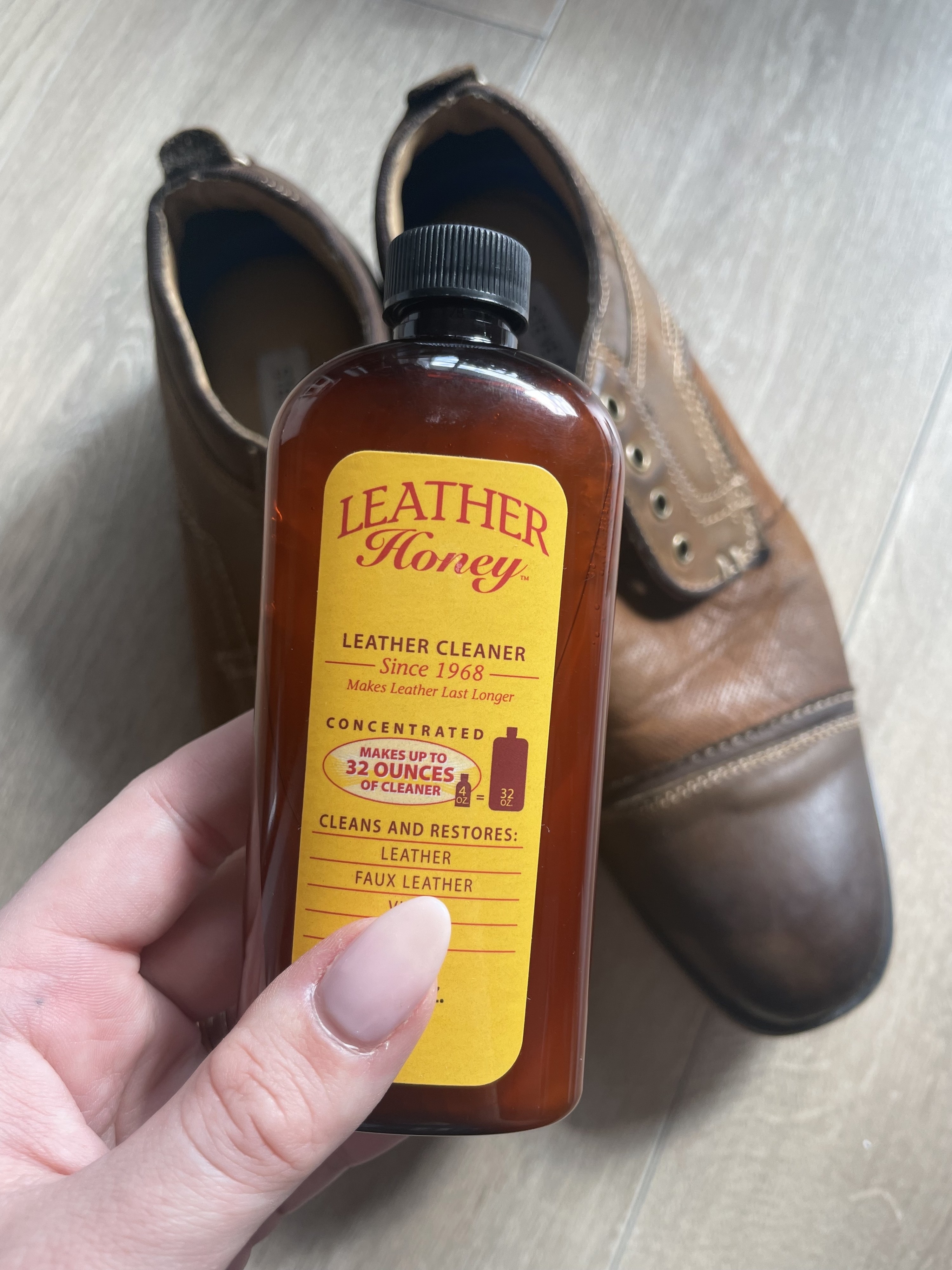a person holding a bottle of the leather honey against a pair of clean leather dress shoes