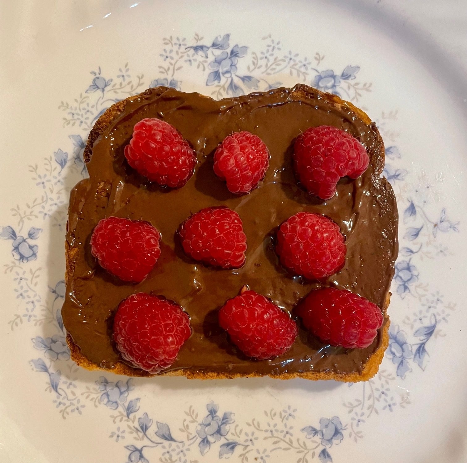 piece of toast covered in hazelnut cocoa spread and sliced raspberries